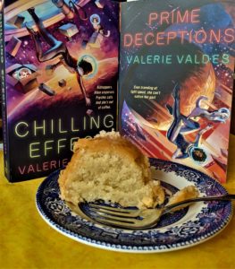 Photo of a slice of cake on a plate with a fork, with the books Chilling Effect and Prime Deceptions in the background