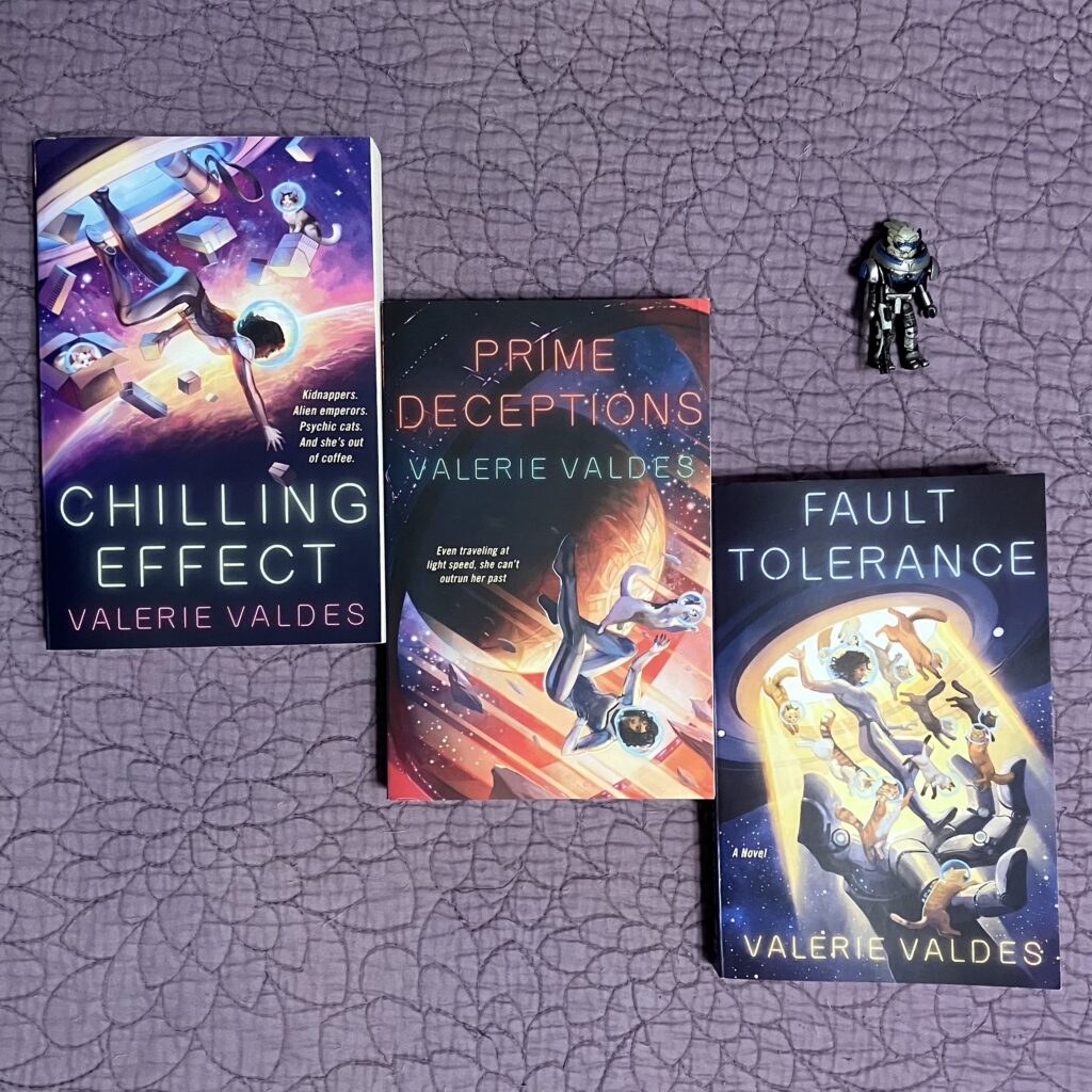 Chilling Effect, Prime Deceptions and Fault Tolerance books arranged on a purple bedspread with a tiny Garrus figure