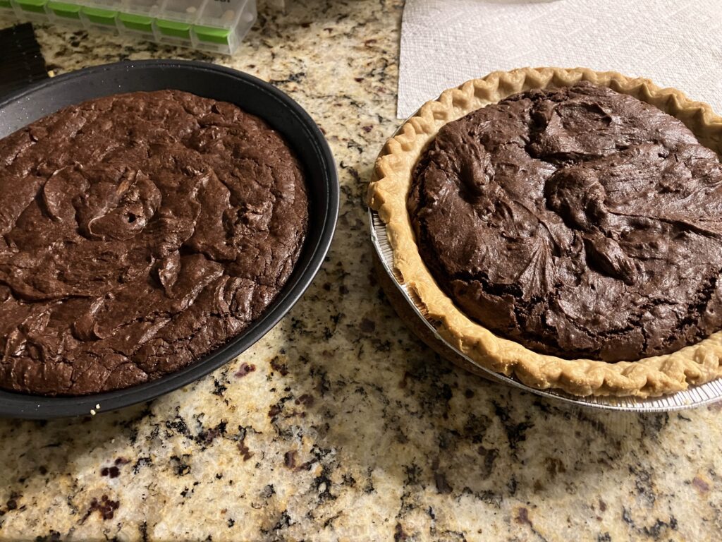 Brownies baked in a round pie tin next to a brownie pie, on a granite countertop, with a peek of my daily pill container in the upper left corner and a random paper towel in the upper right